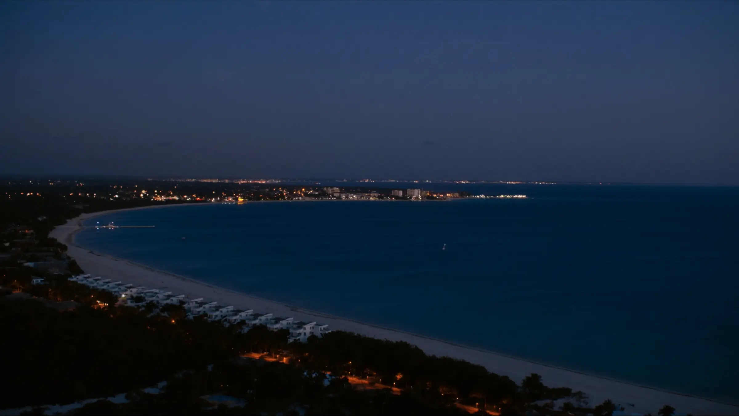 A Caribbean bay at dusk, city lights along the horizon