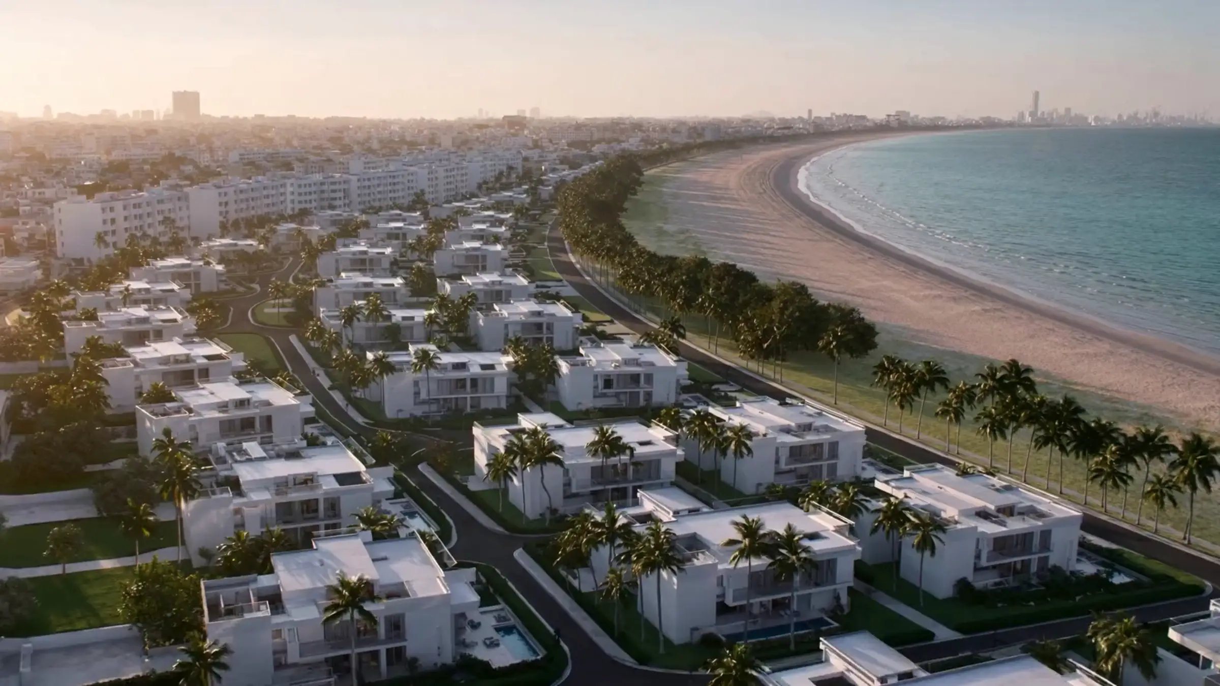 Aerial view of a coastal residential development at sunset, with white villas, palm trees and the sea beyond
